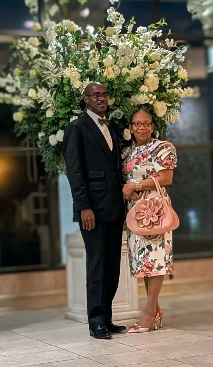 Bishop Leroy and Pastor Herma Hawthorne, dressed formally, standing beneath an arrangement of white roses